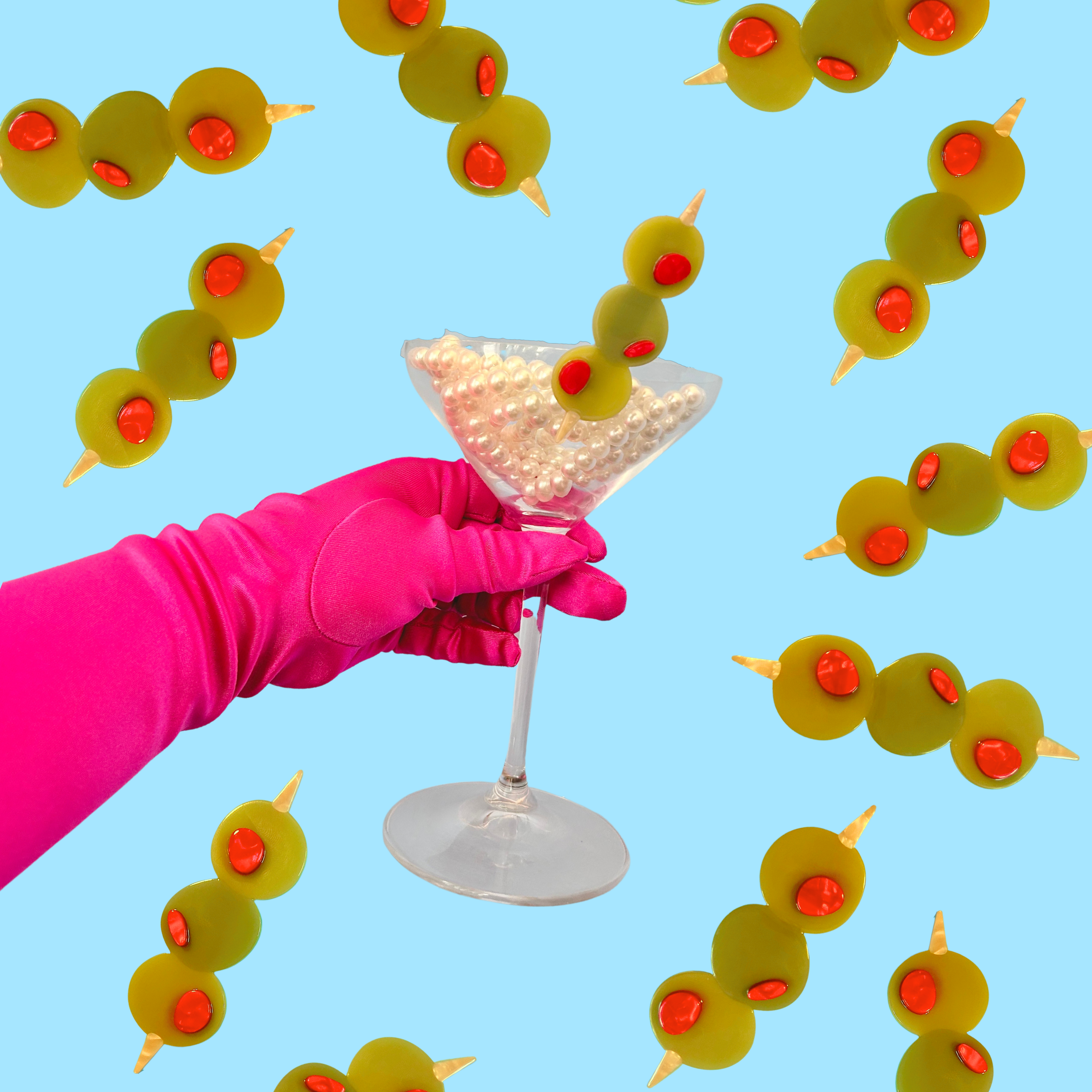 hot pink gloved hand holding martini glass filled with a string of pearls and a martini-olive inspired hairclip by the peach fuzz