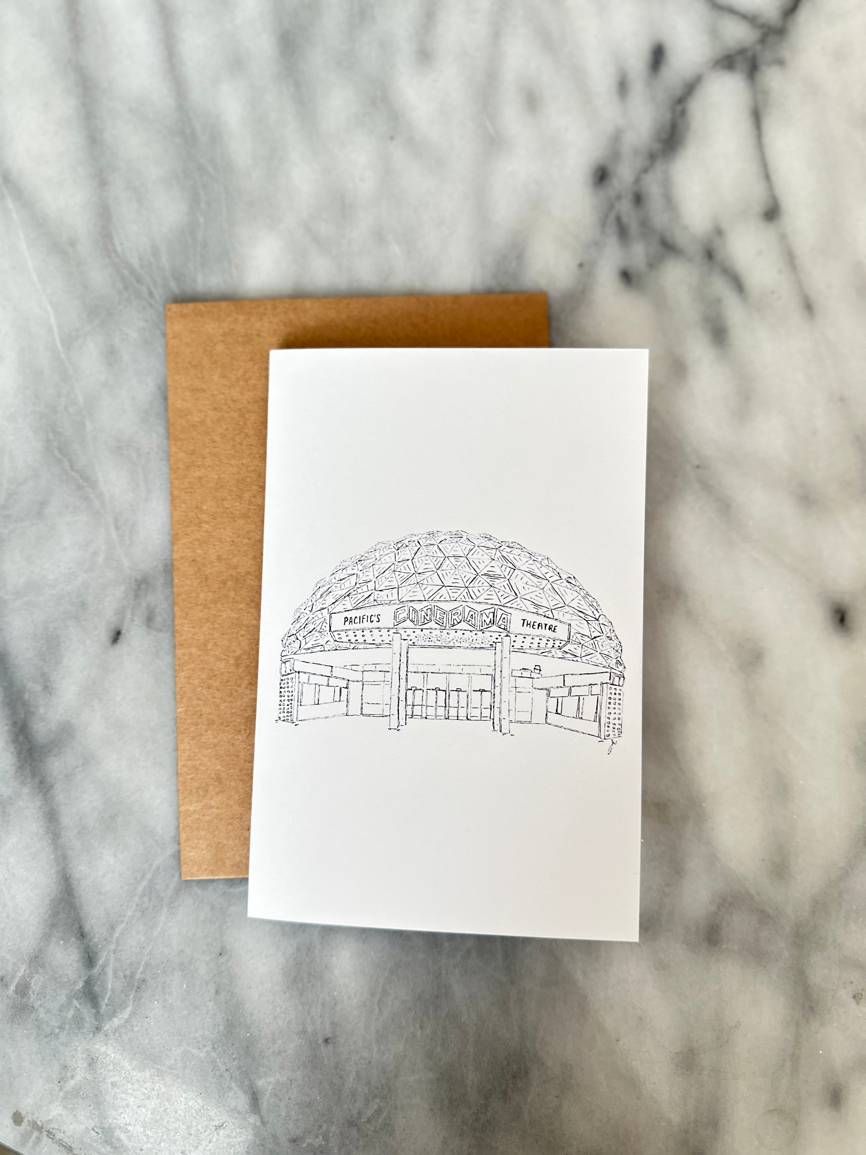 White card with black architectural drawing of the hollywood cinerama on a marble surface