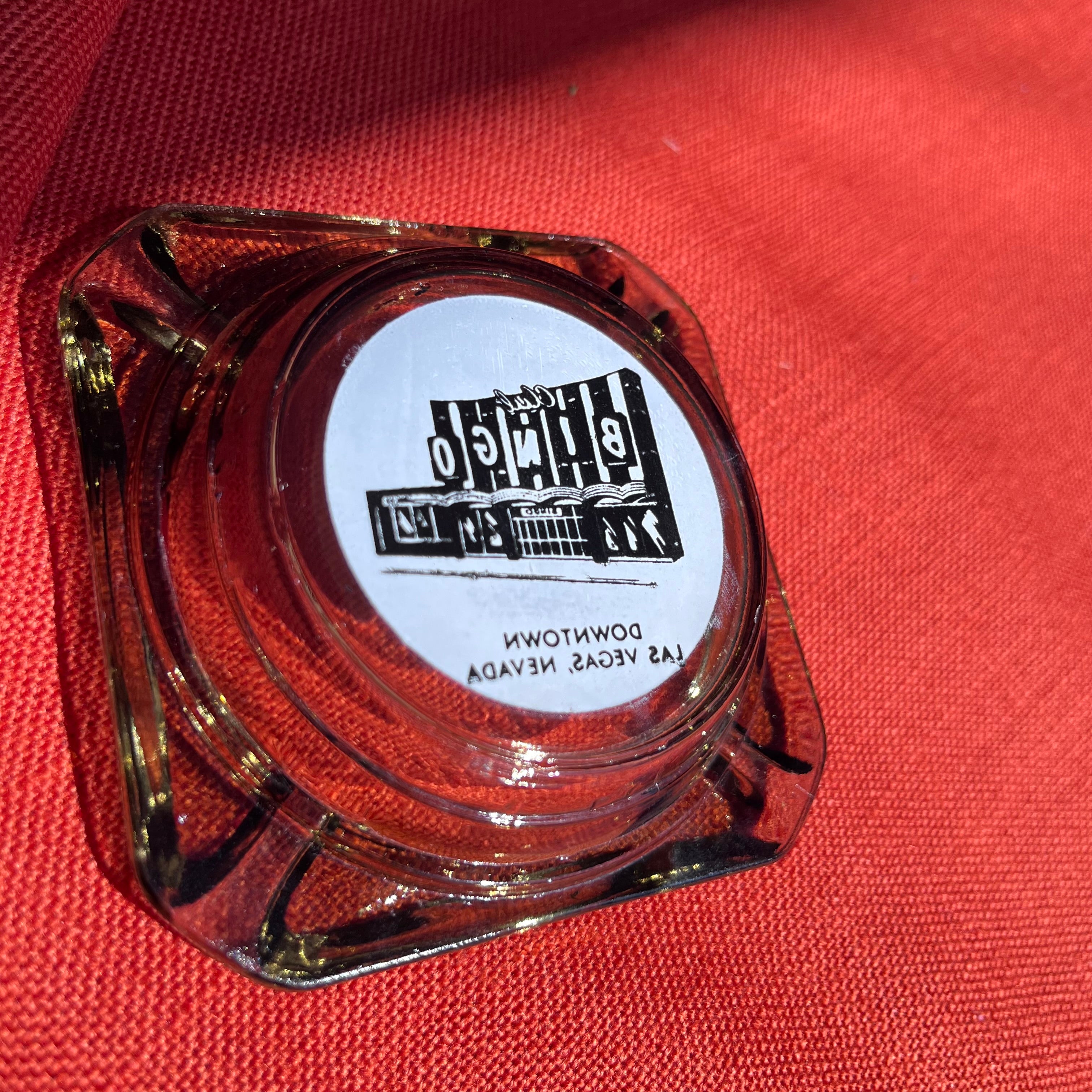 Clear glass ashtray with a logo on a red fabric background