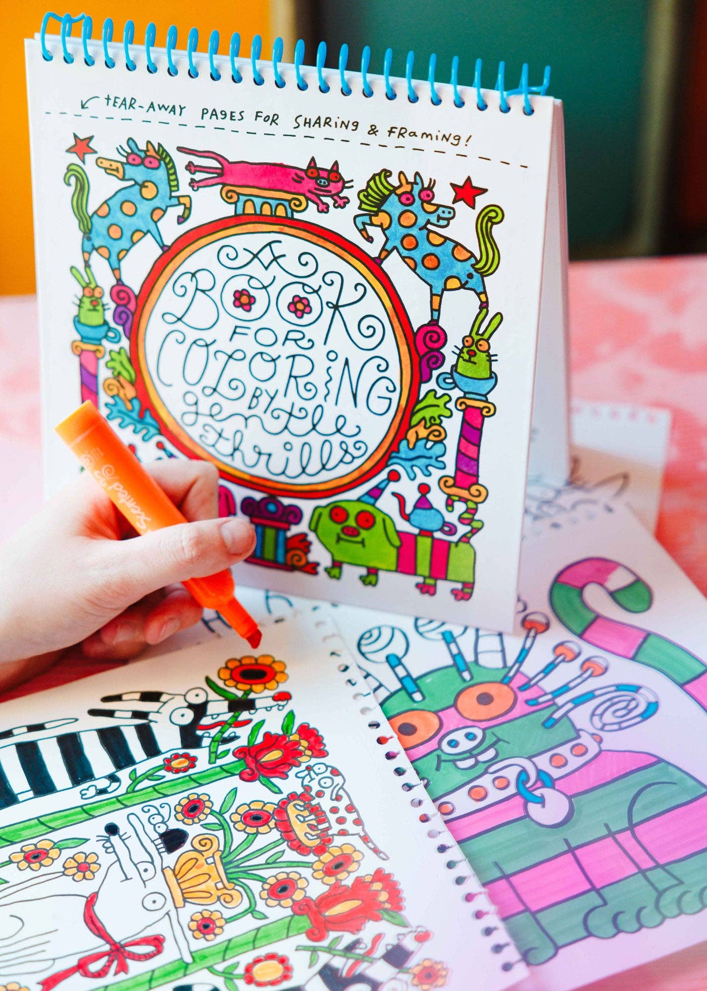 Coloring book with colorful illustrations and a hand holding a marker.
