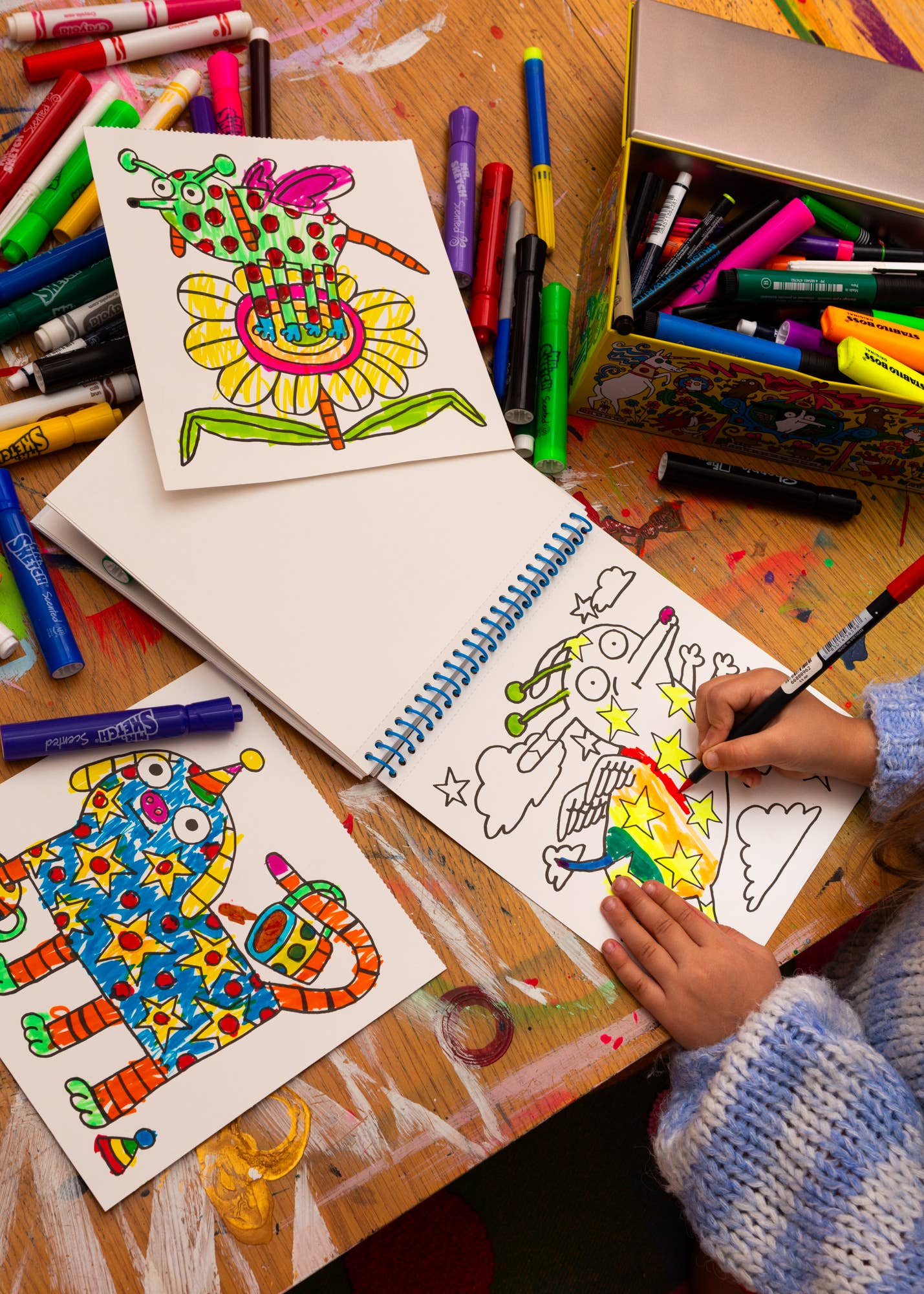 Colorful children's drawings on paper with crayons and a coloring book on a wooden table.