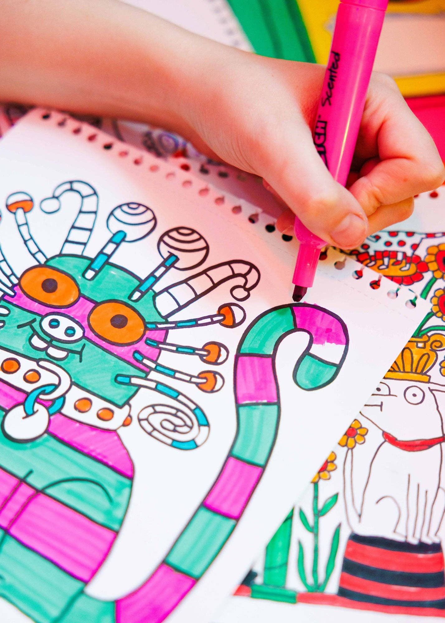 Colorful children's coloring book with a child's hand using a pink marker.