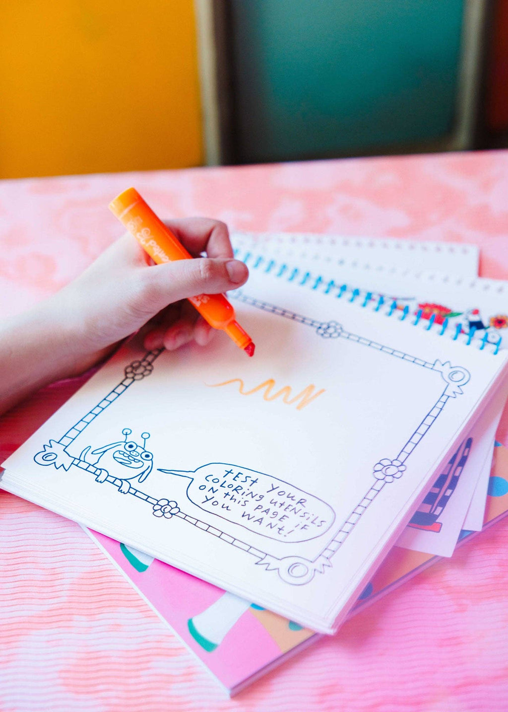 Hand holding a pen over a coloring book with colorful background