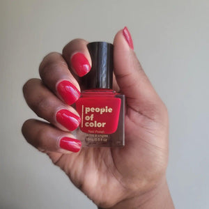 A hand with beautiful brown skin, holding a bottle of red nail polish 