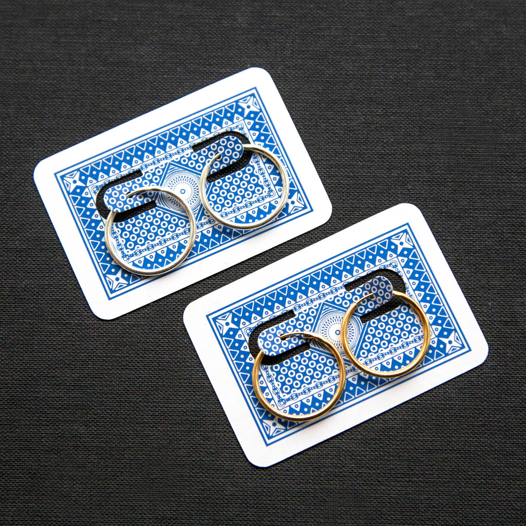 Two pairs of hoop earrings, attached to playing cards with blue and white designs on a black background