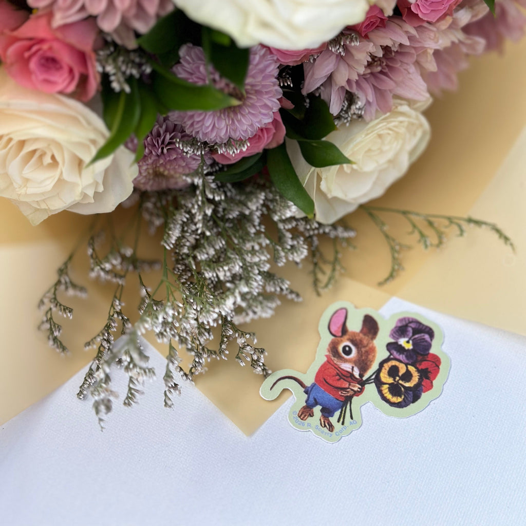 Bouquet of pink, white, and purple flowers with a small card featuring a cartoon character on a yellow background.