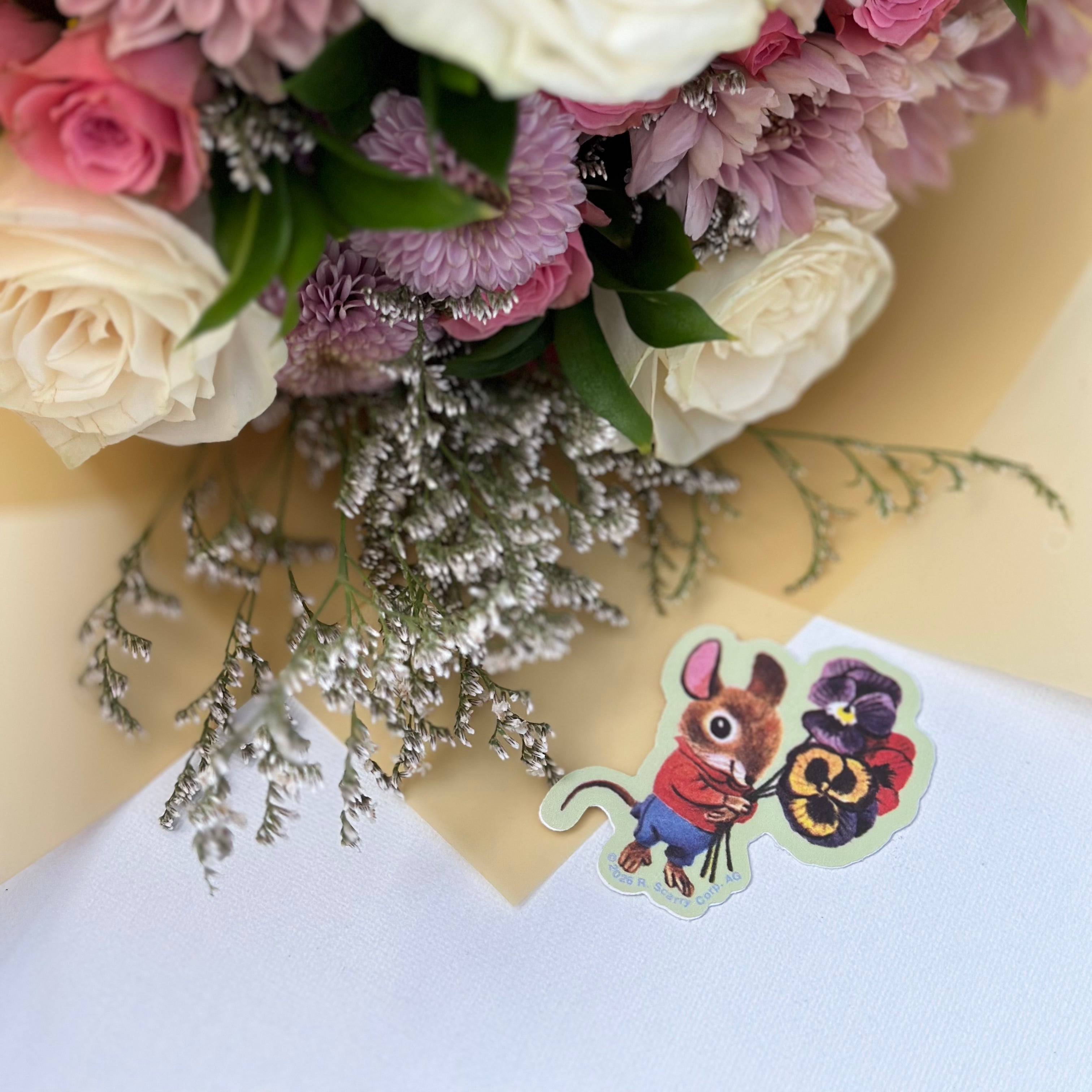 Bouquet of pink, white, and purple flowers with a small card featuring a cartoon character on a yellow background.