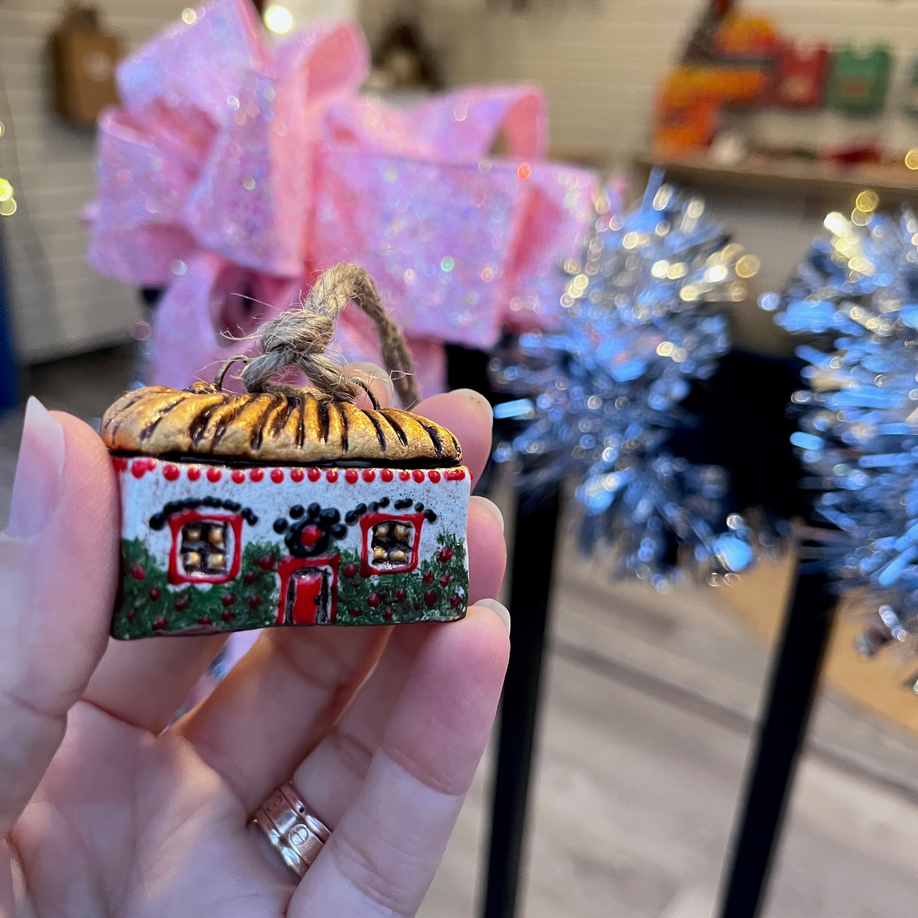 Hand holding a small decorated traditional Ukranian house ornament with a pink bow in the background