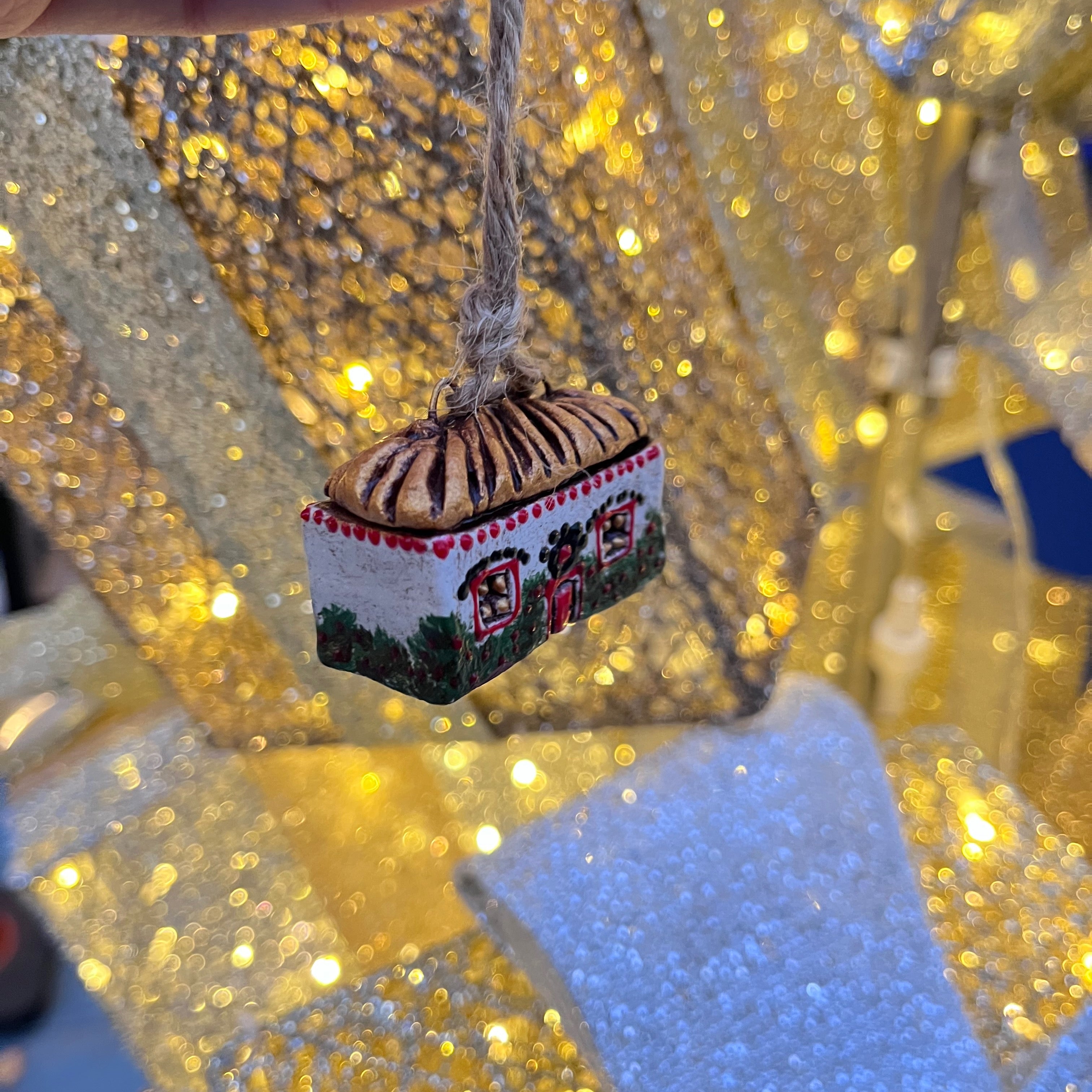 Handmade traditional ukranian house christmas ornament against a glittery gold background.