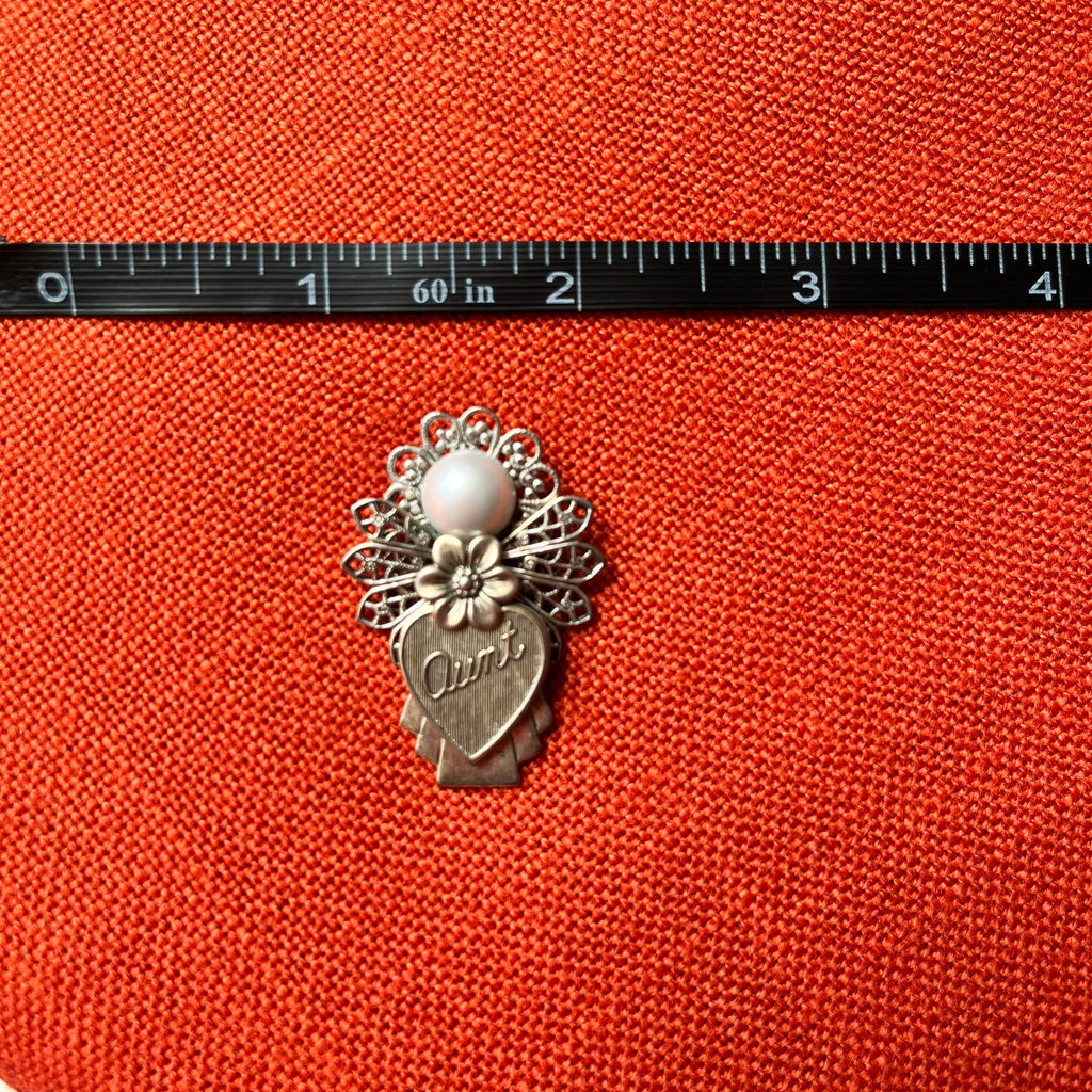 Decorative brooch with a heart and floral design on an orange fabric background, measured against a ruler.