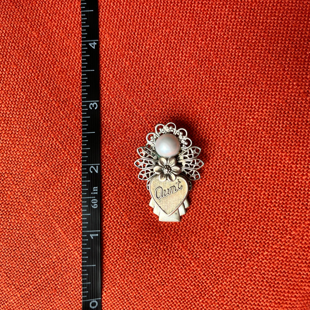 Silver charm with a heart and floral design on an orange fabric background with a ruler for scale.
