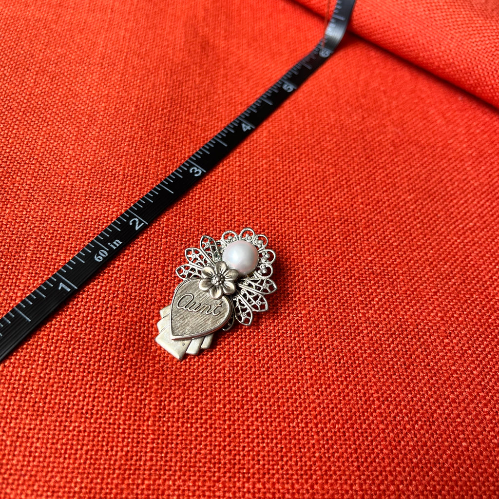 Silver charm with floral design on a red fabric background