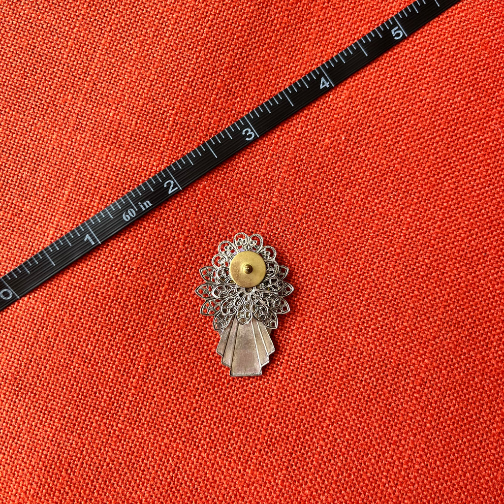 Decorative brooch on an orange fabric background with a ruler for scale.