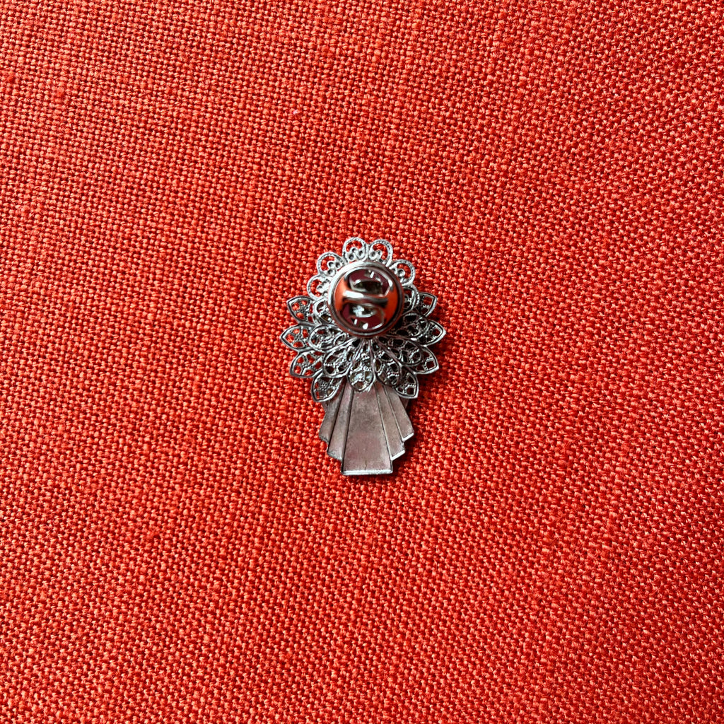 Silver brooch with decorative elements on a red fabric background